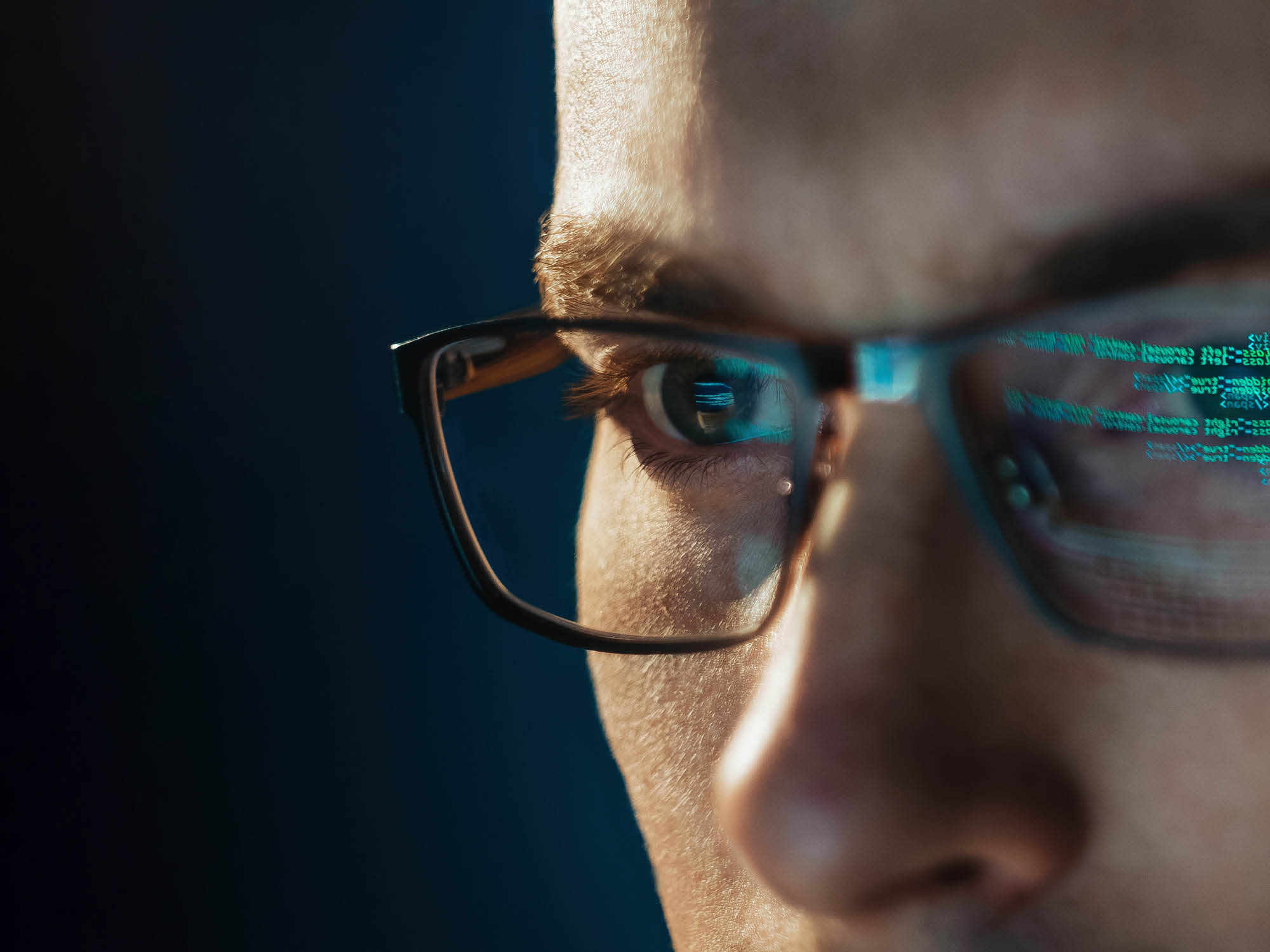 Close-up portrait of focused software engineer wearing eyeglasses looking at computer screen working with big data. Programming code reflecting in glasses. Data science, Machine Learning, AI concept